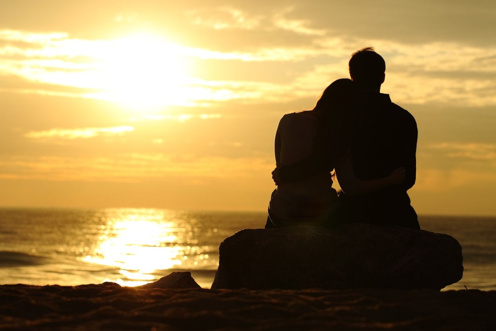 The couple sits hugging at sunset